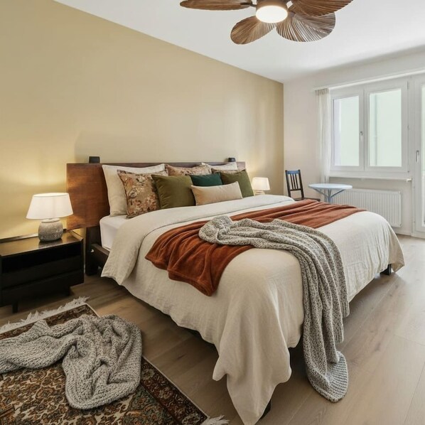 A bedroom with a bed, nightstands, a lamp, a chair, a window, and a ceiling fan.