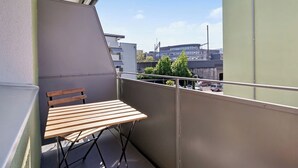 A balcony with a wooden table and a bench, overlooking a cityscape with buildings and parked cars. - Studio w/ Balcony & Modern Amenities (202-16) (Zürich)