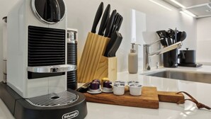 A modern kitchen with a Delonghi espresso machine, a wooden cutting board, and a knife block. - Studio w/ Balcony & Modern Amenities (202-16) (Zürich)