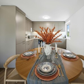 Un espace repas moderne avec une table ronde dressée pour quatre personnes, agrémenté d’un vase avec des branches oranges, de bougies blanches et de vaisselle à motifs.