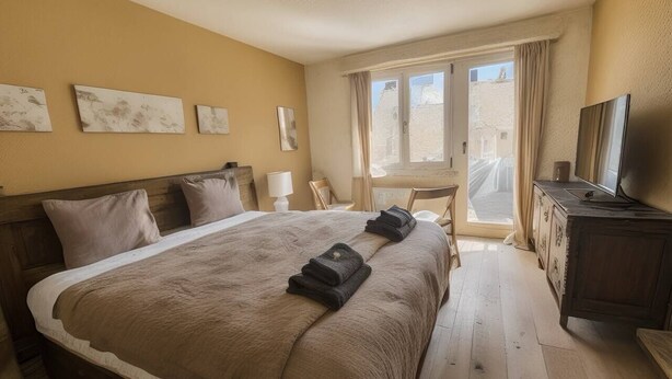 Een slaapkamer met een groot bed, een houten hoofdbord, een televisie, een bureau en een raam met gordijnen.
