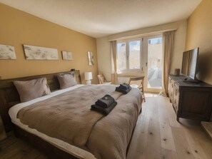 A bedroom with a large bed, a wooden headboard, a TV, a desk, and a window with curtains. - Elegant Studio in Zurich w/ Balcony (302-16) (Zürich)