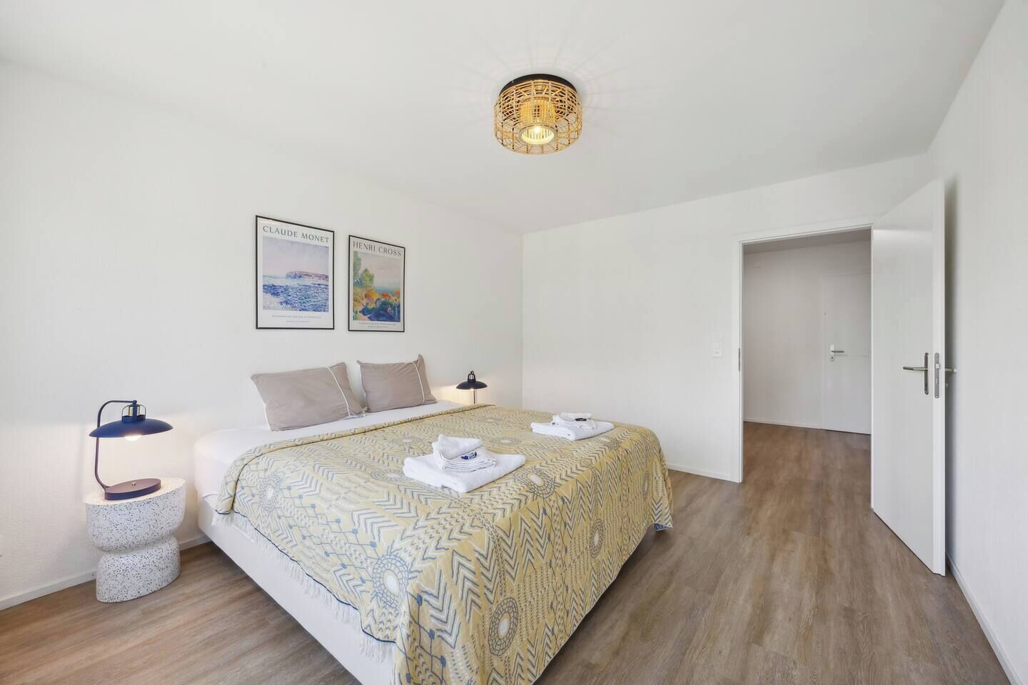 A modern bedroom with a bed, two wall-mounted paintings, a bedside lamp, and a door leading to another room.