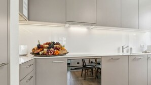 Een moderne keuken met witte kastjes, een inbouwoven en een schaal fruit op het aanrecht.