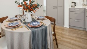 Een eethoek met een ronde tafel gedekt voor vier personen, met blauwe en witte borden, gouden bestek en een middelpuntstuk met oranje bessen en groene bladeren.