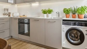 Een moderne keuken met grijze kastjes, een inbouwoven, een wasmachine en potplanten op het aanrecht.