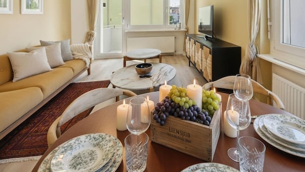 A cozy living room with a sofa, a dining table set with plates and glasses, and a TV on a cabinet.