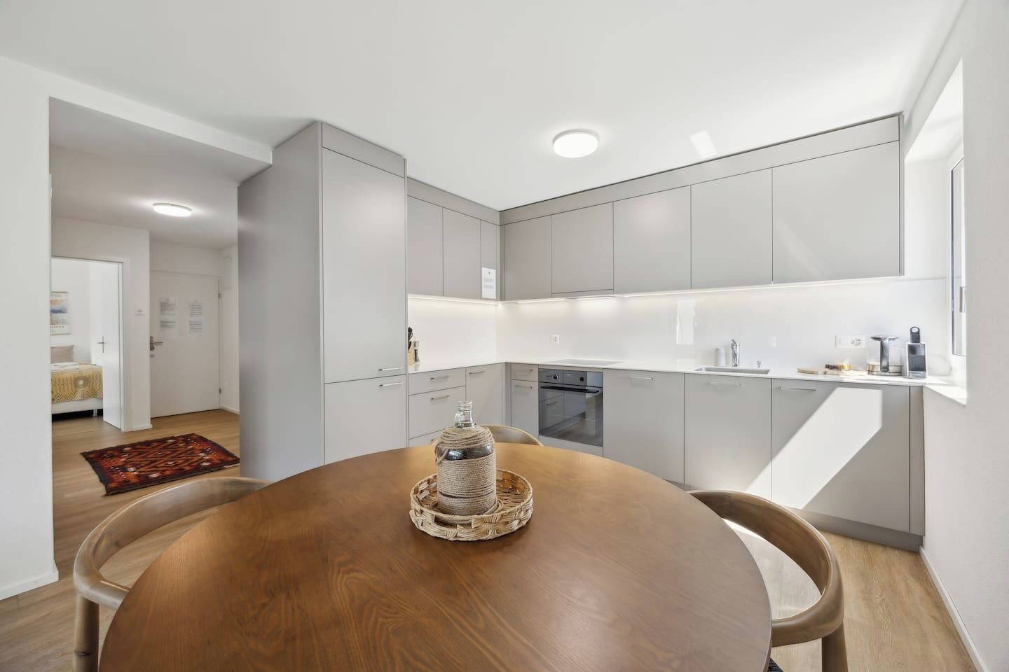 A modern kitchen with white cabinetry, a wooden dining table, and a built-in oven.