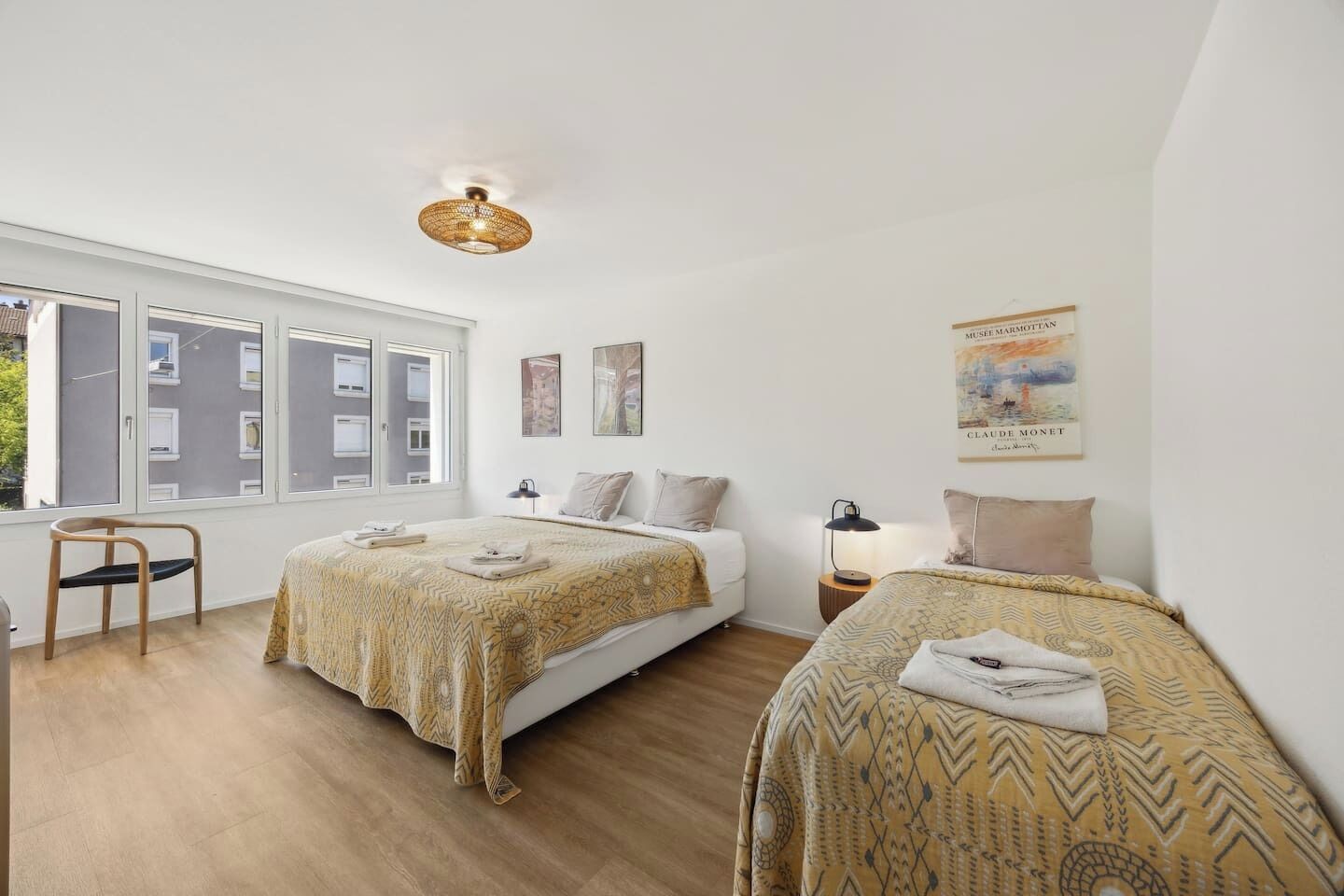 A modern bedroom with two beds, a large window, and artwork on the walls.