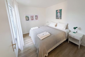 Quarto com cama, mesa de cabeceira, abajur e três obras de arte emolduradas na parede.