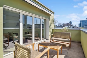 A balcony with wicker furniture, a sliding glass door, and a city view. - Rooftop Suit in Zürich Oerlikon! (401) (Zürich)