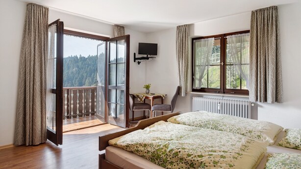 Een slaapkamer met een bed, een bureau, een stoel, een televisie en een balkon met uitzicht.