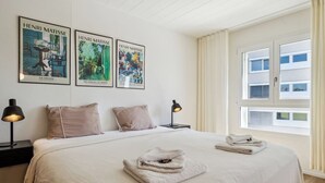 Une chambre d’hôtel avec un grand lit, deux tables de chevet avec des lampes, trois affiches d’Henri Matisse et une fenêtre avec des rideaux.