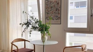 Une pièce comprenant deux chaises en bois, une petite table ronde, une plante en pot et un tableau encadré accroché au mur.