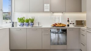 Une cuisine moderne avec des armoires grises, un lave-vaisselle encastré et un four à micro-ondes. On peut voir des plantes en pot sur le comptoir, ainsi qu’une bouteille de vin et des verres sur la droite.