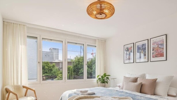 Une chambre à coucher avec un grand lit, une chaise, une fenêtre avec des rideaux et des tableaux encadrés accrochés au mur.