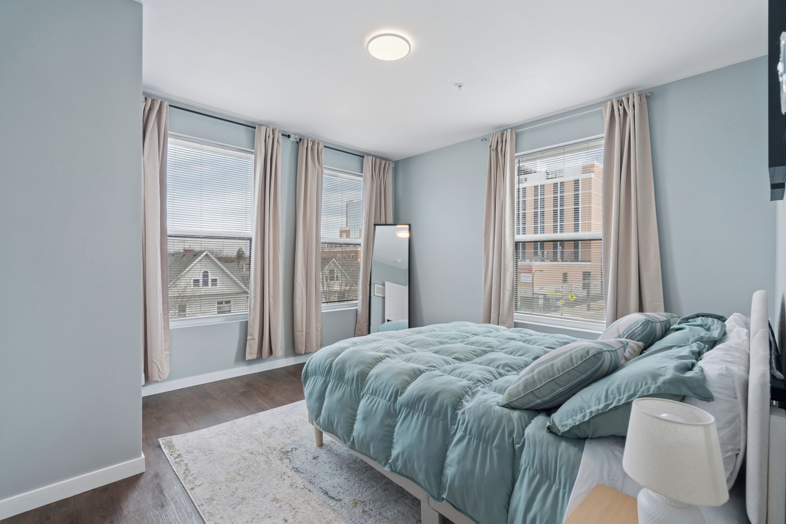 A bedroom with a bed, a nightstand, a mirror, and a window with curtains.