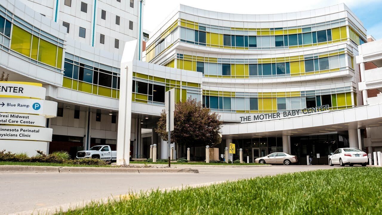 A modern building with multiple entrances, including a prominent sign for 'The Mother Baby Center.'