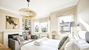 Habitación de hotel con cama, sofá, estantería, ventana con vistas y lámpara colgante.
