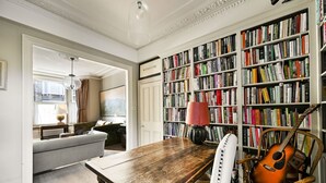 Ein Zimmer mit einem Holztisch, einem Stuhl, einem Bücherregal und einer Gitarre.