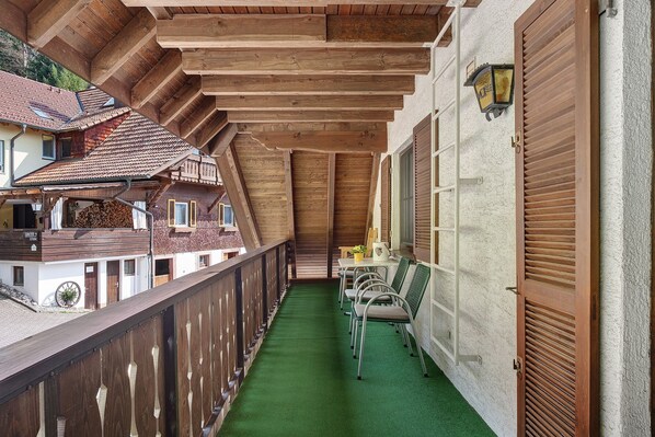 A covered balcony with a green floor, wooden ceiling beams, and a view of adjacent buildings. - Apartment 5 with Balcony, Barbecue Area and Wi-Fi (Oberharmersbach)