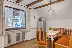 A dining area with a table, chairs, a radiator, a window with curtains, a cross on the wall, and a hanging light fixture. - Apartment 5 with Balcony, Barbecue Area and Wi-Fi (Oberharmersbach)