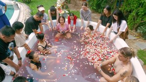 Un groupe de personnes est rassemblé en cercle autour d’une piscine remplie d’eau et de pétales de fleurs.