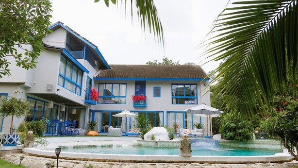Un bâtiment à deux étages doté d’une piscine, d’un espace extérieur aménagé et de plantes tropicales.