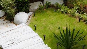 Un chemin en bois peint en blanc, traversant un jardin parsemé de rochers et de plantes.