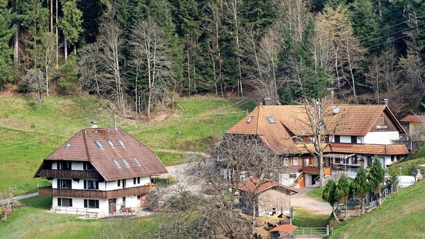 Un immeuble à plusieurs étages, doté d’un toit en pente, d’un balcon et d’une petite structure adjacente.