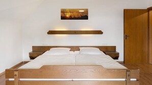 Une chambre à coucher avec un lit en bois, une table de chevet, une étagère fixée au mur et une porte.