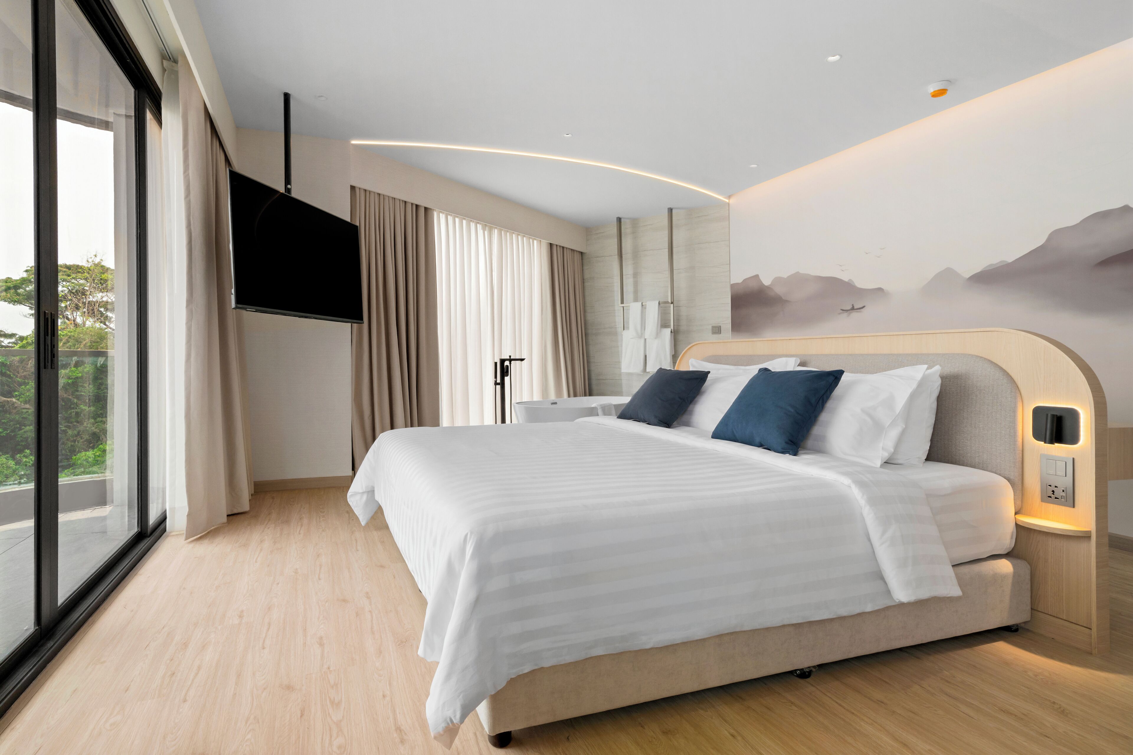 Habitación de hotel moderna con una cama grande, un televisor de pantalla plana, vistas al exterior y un diseño minimalista.
