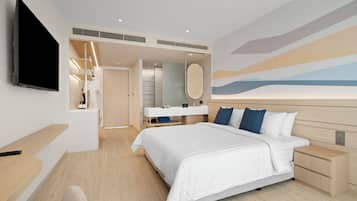 Una habitación de hotel moderna con una cama grande, un televisor montado en la pared, un tocador con espejo y un baño visible a través de una puerta abierta.