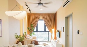 A hotel room with a dining area, a ceiling fan, an air conditioning unit, a large window with curtains, and a view of the cityscape. - SKYLINE KL By The Stay Hub (Kuala Lumpur)