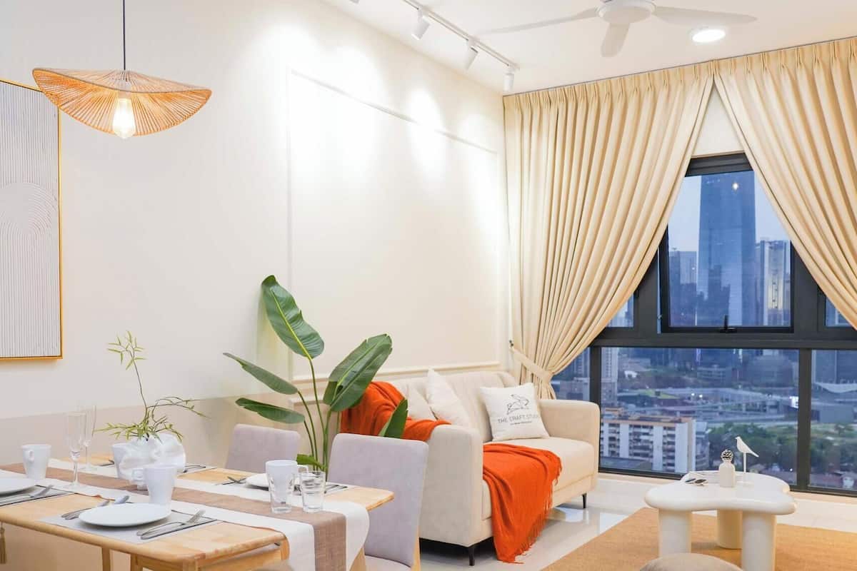 Een moderne woonkamer met een eethoek, grote ramen met gordijnen en uitzicht op de stad.