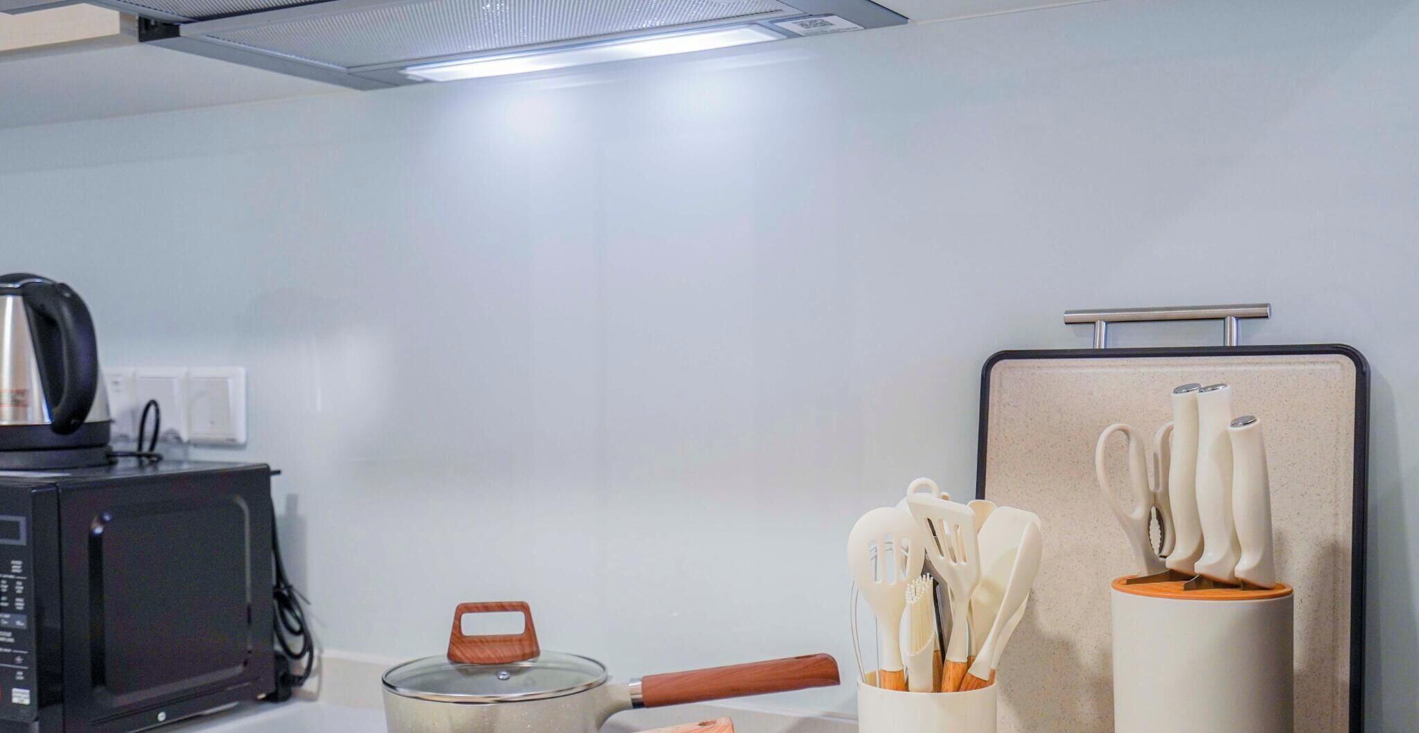 A kitchenette with a microwave, kettle, pot, and utensils.