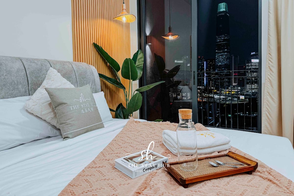 Een moderne slaapkamer met uitzicht op de stad, een bank, een nachtkastje met dienblad en een decoratieve plant.