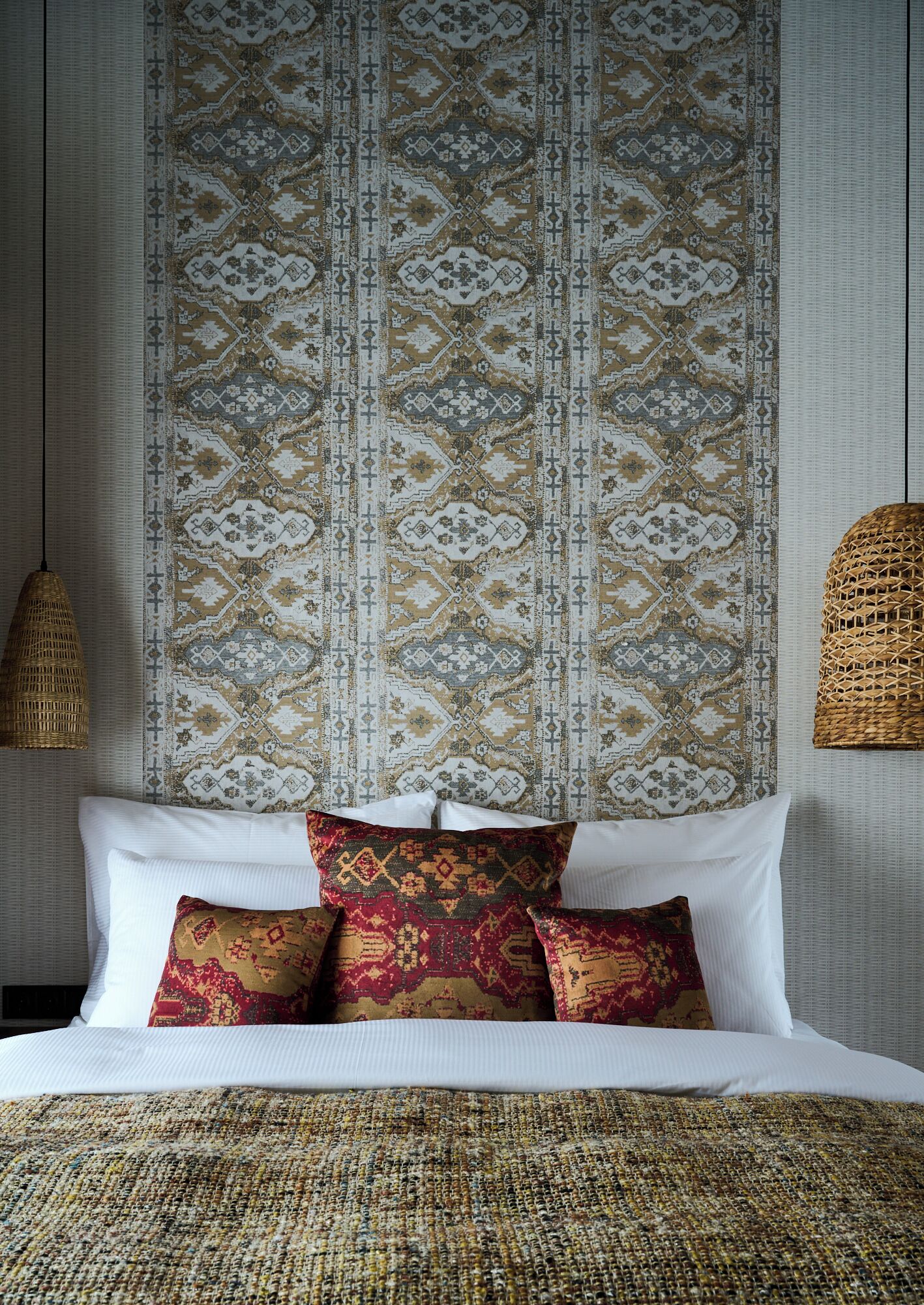 A neatly made bed with patterned pillows and a woven blanket, set against a wall with a decorative headboard.