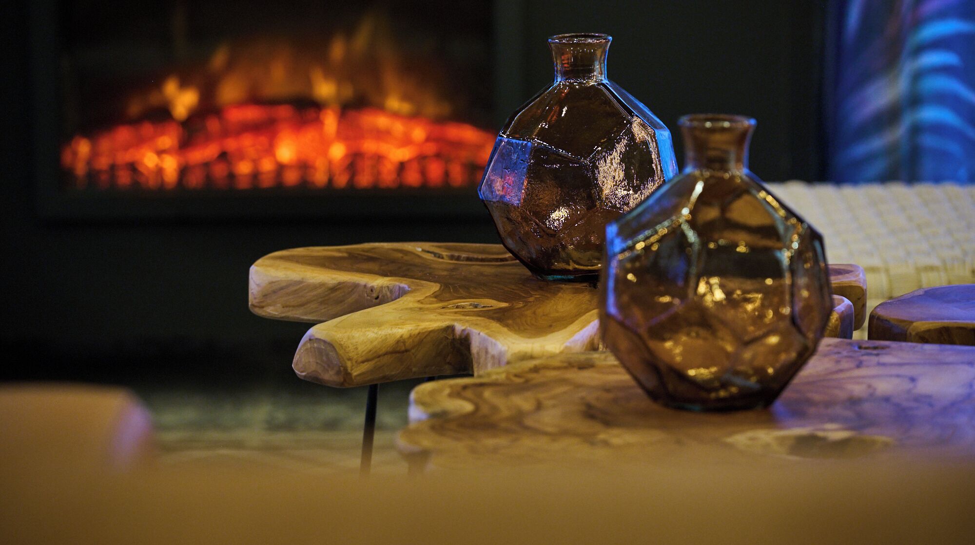 Two glass vases on wooden stands with a fireplace in the background.