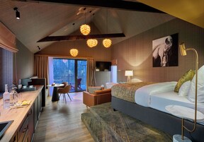 A modern hotel room with a large bed, a desk, and a dining area.