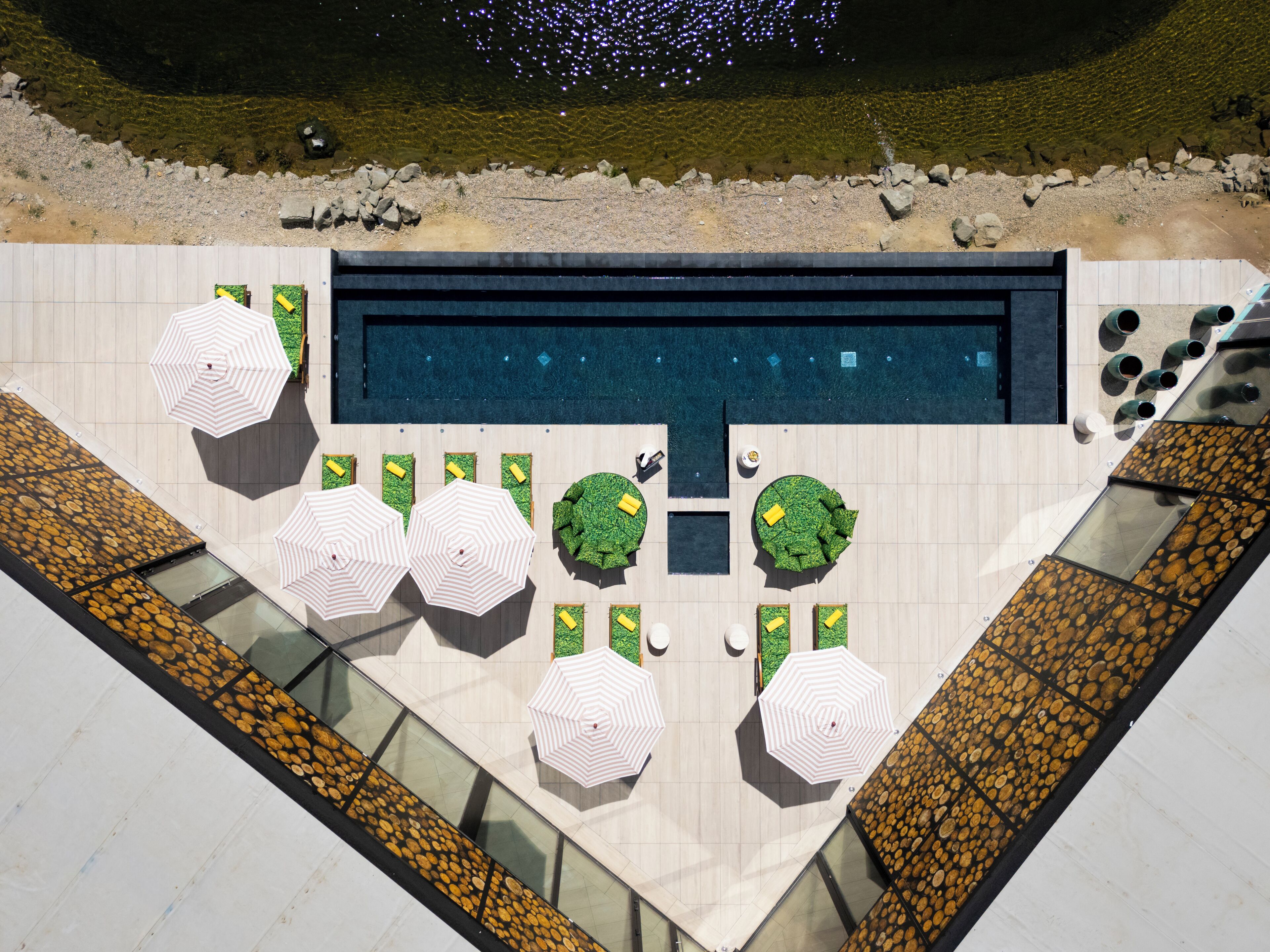 Vista aérea de un moderno espacio de piscina con una pileta rectangular, múltiples sillas de descanso y sombrillas.