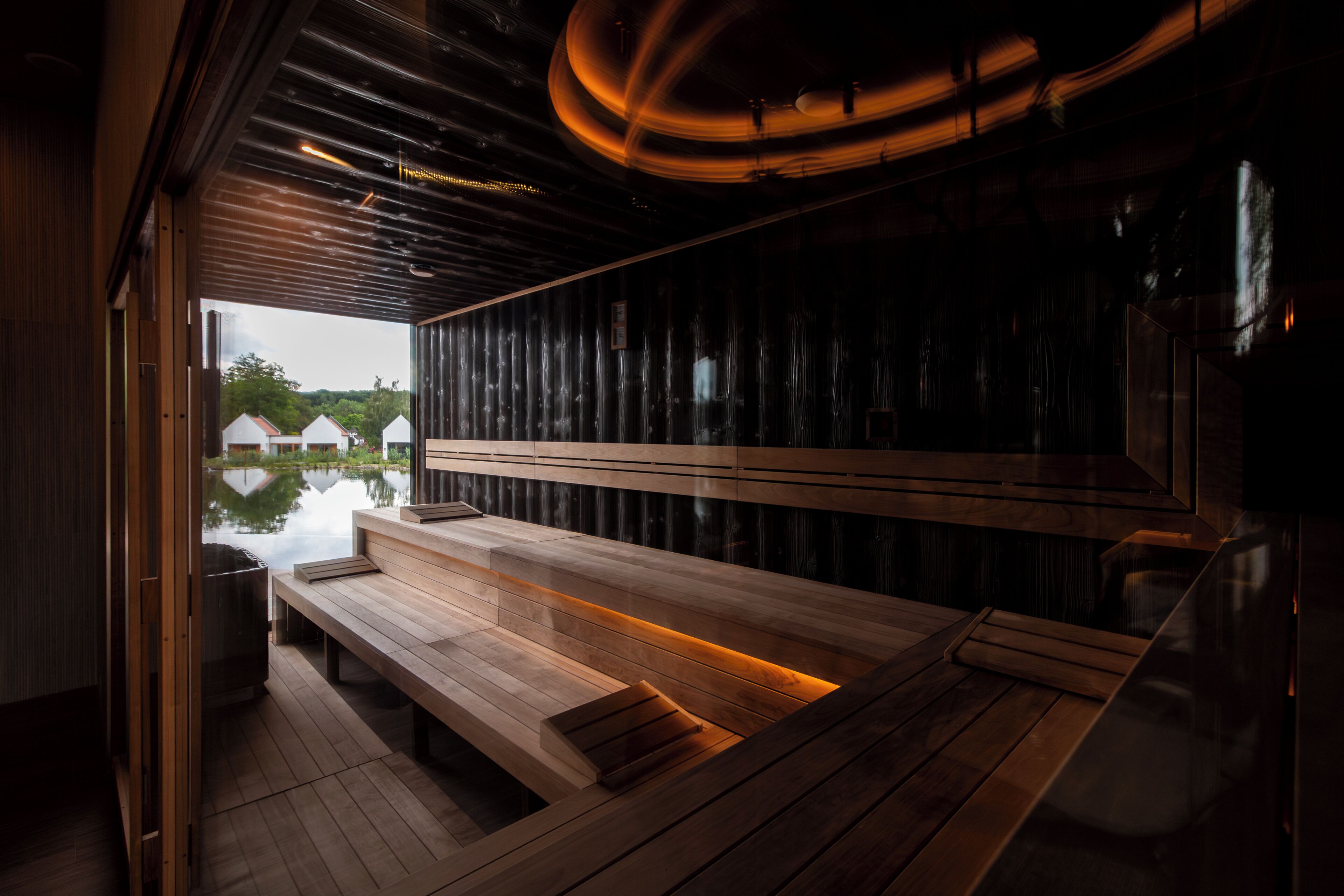 A sauna with wooden benches and a view of houses through a large window.