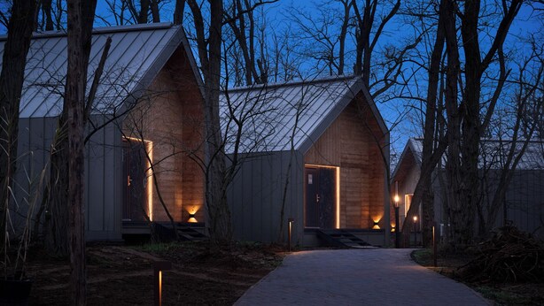 A row of modern, wooden cabins with sloped roofs, each featuring a lit entrance and a pathway leading to them.