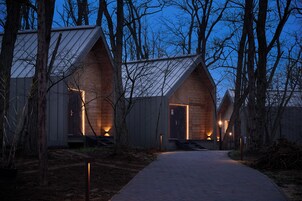 A row of modern, wooden cabins with sloped roofs, each featuring a lit entrance and a pathway leading to them.