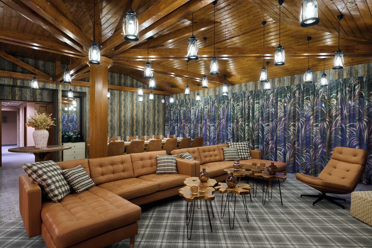 A spacious room with a large sectional sofa, multiple dining tables, and a patterned wall.