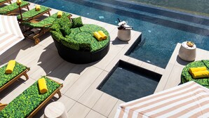 A pool area with lounge chairs, a hot tub, and a view of a lake with houses in the background.