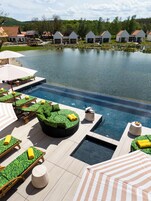 A pool area with lounge chairs, a hot tub, and a view of a lake with houses in the background.
