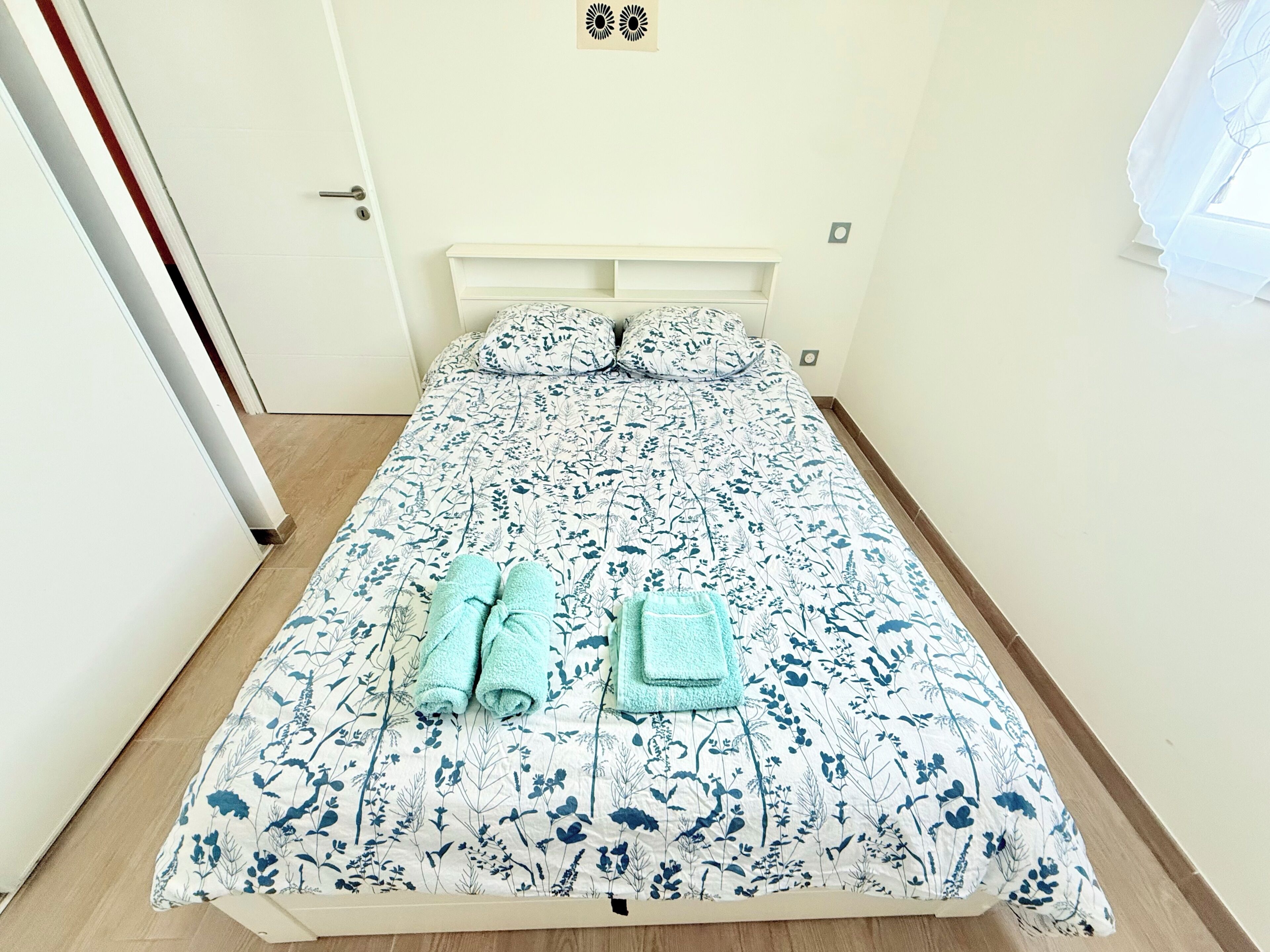 Ein Bett mit einem blumigen Bettüberwurf, zwei gefaltete Handtücher und ein weißes Kopfteil.