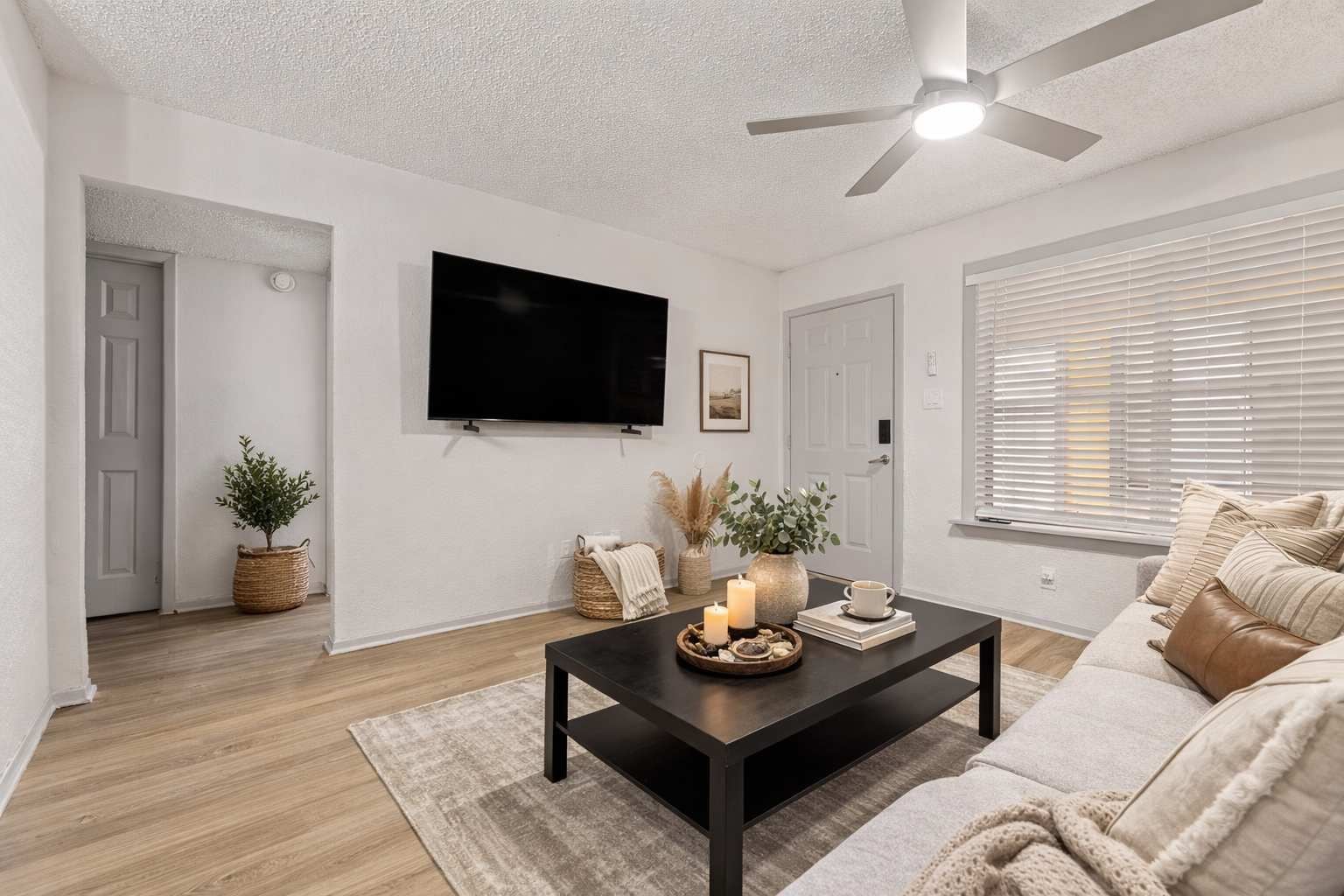 A modern living room with a flat-screen TV, a ceiling fan, a sofa, and a coffee table with decorative items.