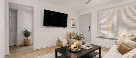 A modern living room with a flat-screen TV, a ceiling fan, a sofa, and a coffee table with decorative items.